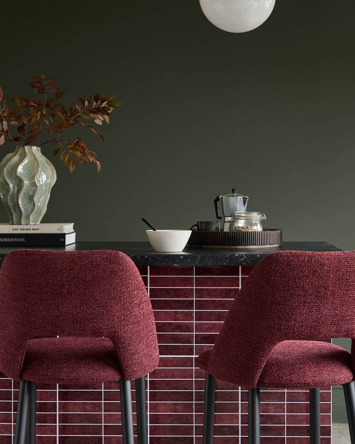 Close-up of two dark red upholstered bar stools with black legs in front of a burgundy tiled counter.