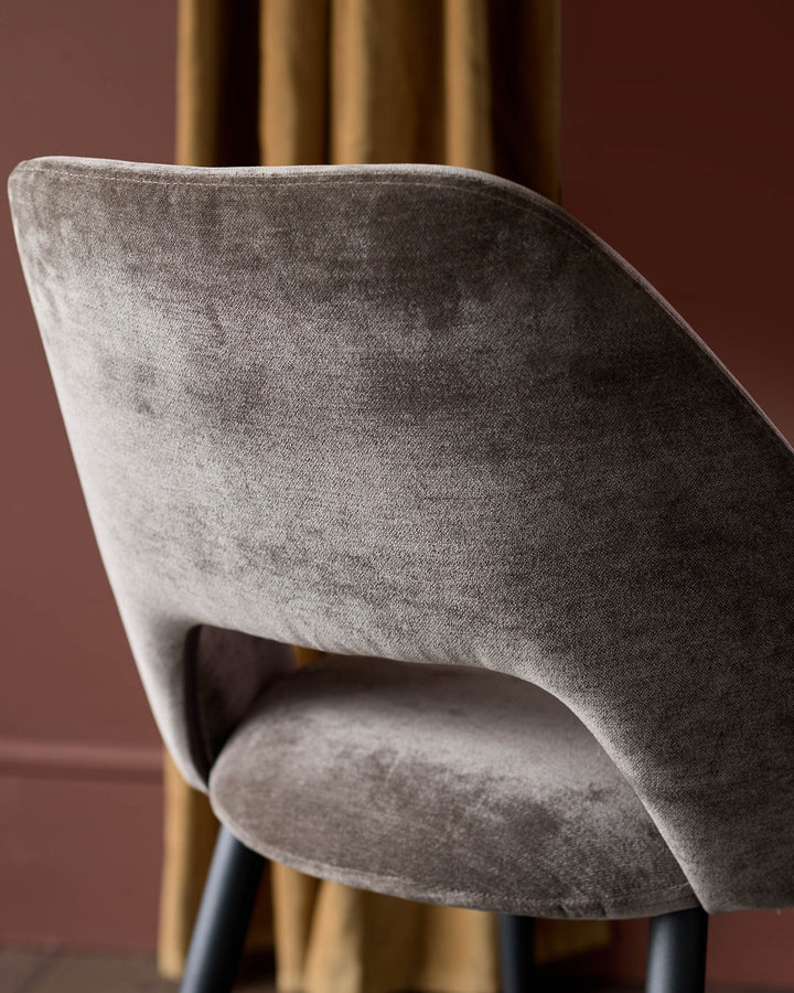 Close-up of a stylish, brown velvet chair with a curved backrest and sleek black legs. Modern design for sophisticated interiors.