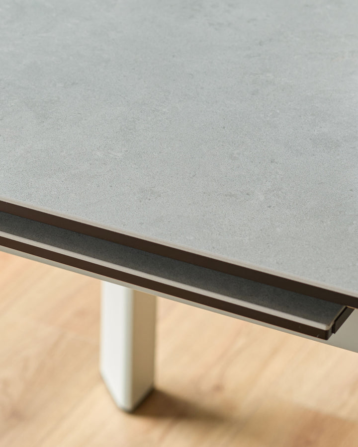 Light grey ceramic extending dining table with dark metal handle detail and white pedestal base, angled close-up view.