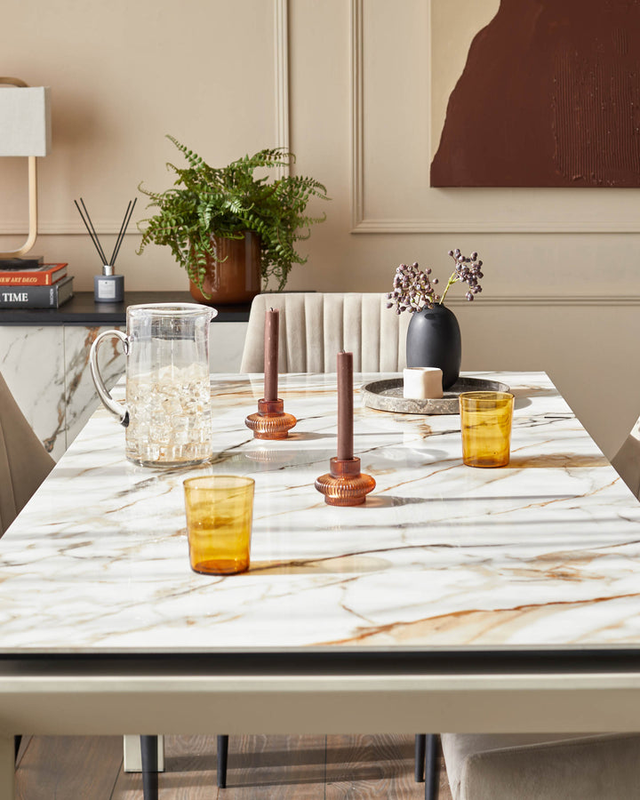 Marble dining table with orange glasses and candles, fern and art displayed behind.