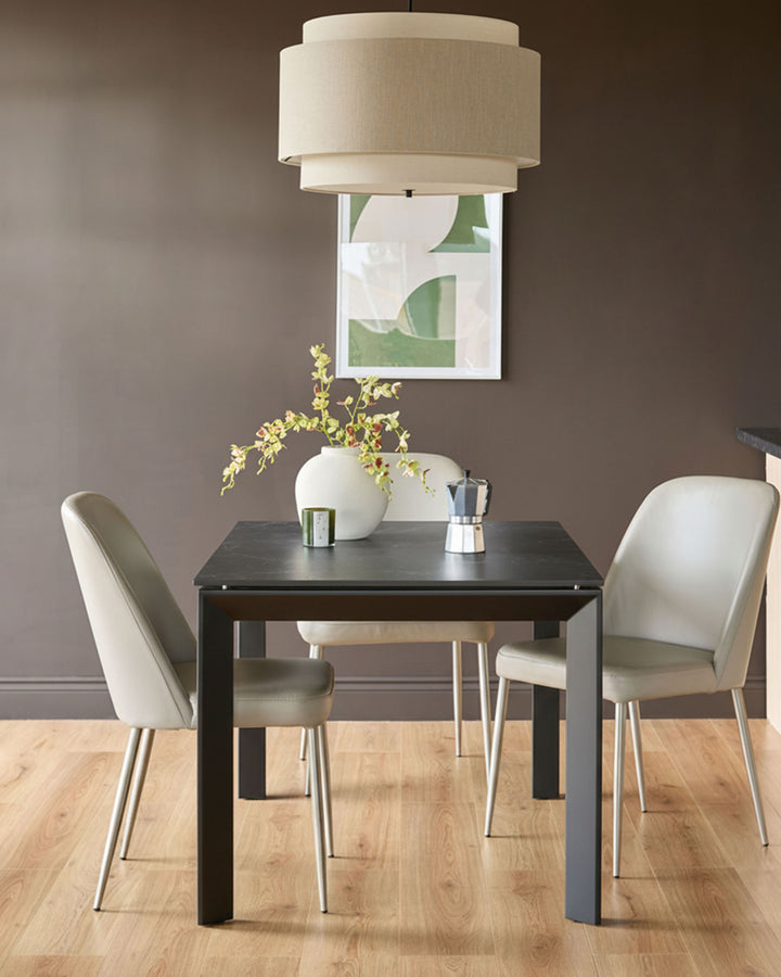 Louis dark grey extending dining table styled with two cream chairs, white vase, pendant light and artwork.