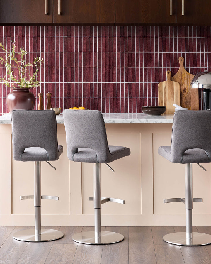 Ludo fabric gas-lift bar stool in dark grey with brushed stainless steel base, shown in kitchen setting.