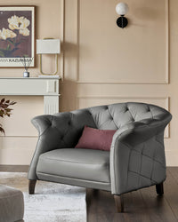 A grey leather armchair with a cushion sits on a rug in front of a fireplace and framed print.
