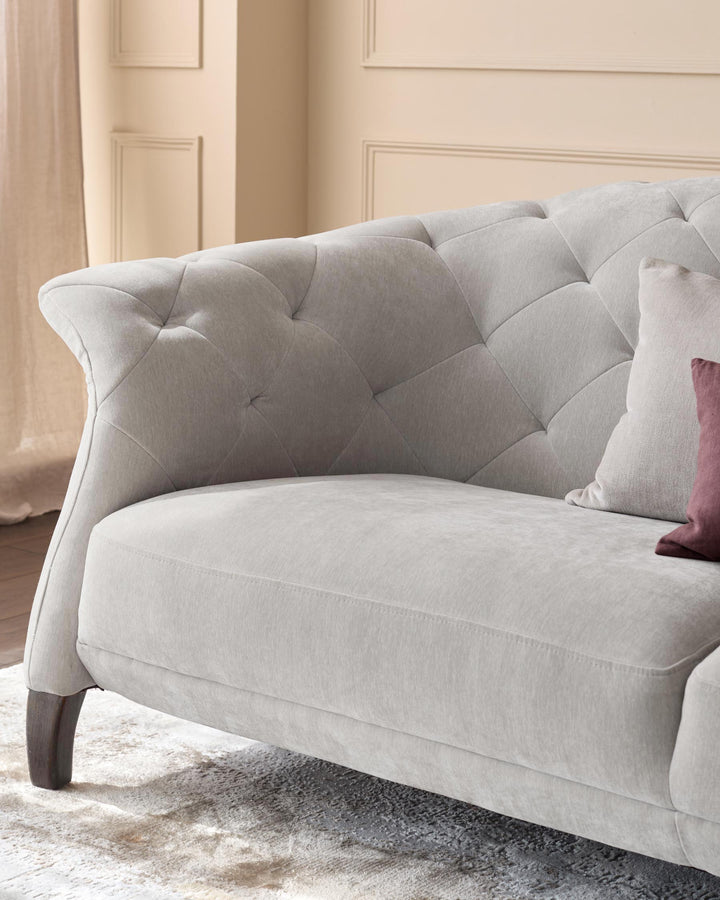 A comfy light grey, button-back sofa with a stylish, curved arm and plush cushions, inviting relaxation.