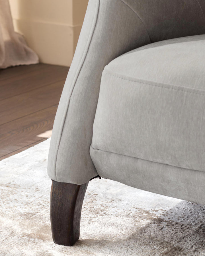 Close-up of a stylish, light grey armchair with a curved armrest and dark wood leg, sitting on a plush rug.