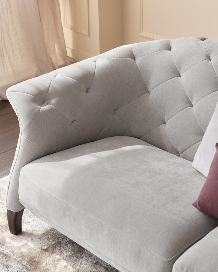 A luxurious, grey, tufted sofa with dark wooden legs, part of a stylish living room set.
