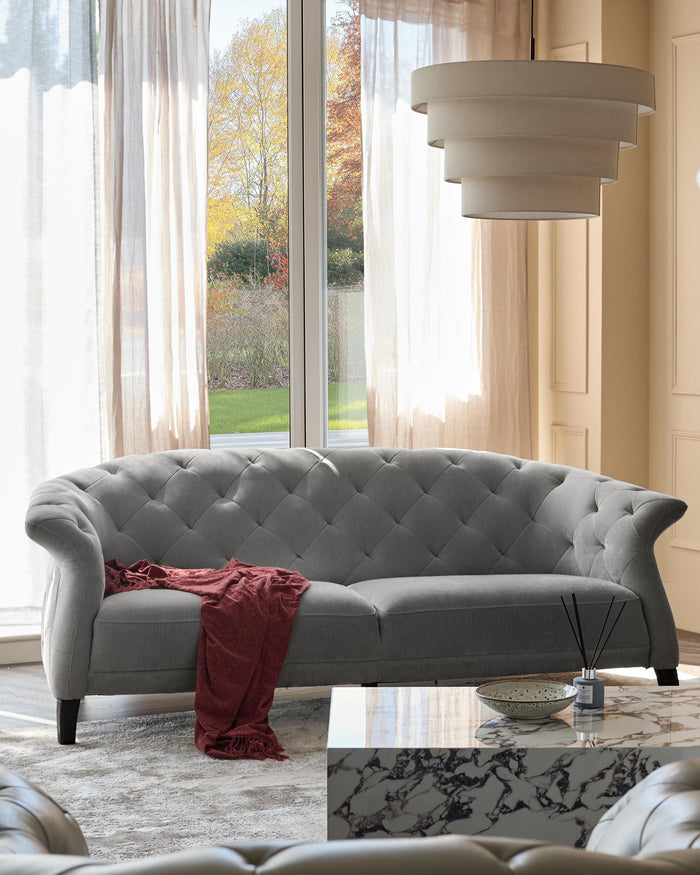 A grey Chesterfield sofa with a throw. The sofa is in a bright living room with a marble table and layered ceiling light.