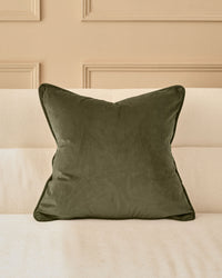 Luca Cushion in Medium Olive Green displayed on a cream striped sofa against a beige paneled wall.