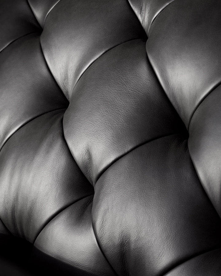 Close-up of a luxurious, deep-buttoned, black leather sofa, showcasing its intricate design and soft texture.
