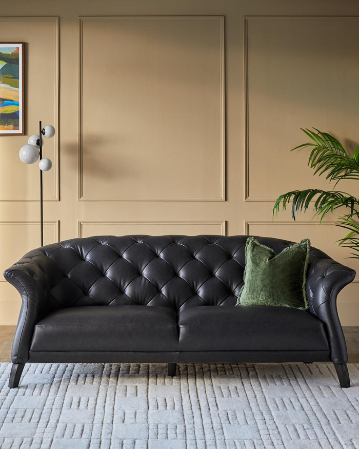 A luxurious black leather Chesterfield sofa, complete with a green velvet cushion, sits on a patterned rug in a stylish living room.