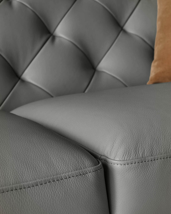 Close-up of a grey leather sofa with button detailing and a tan pillow.