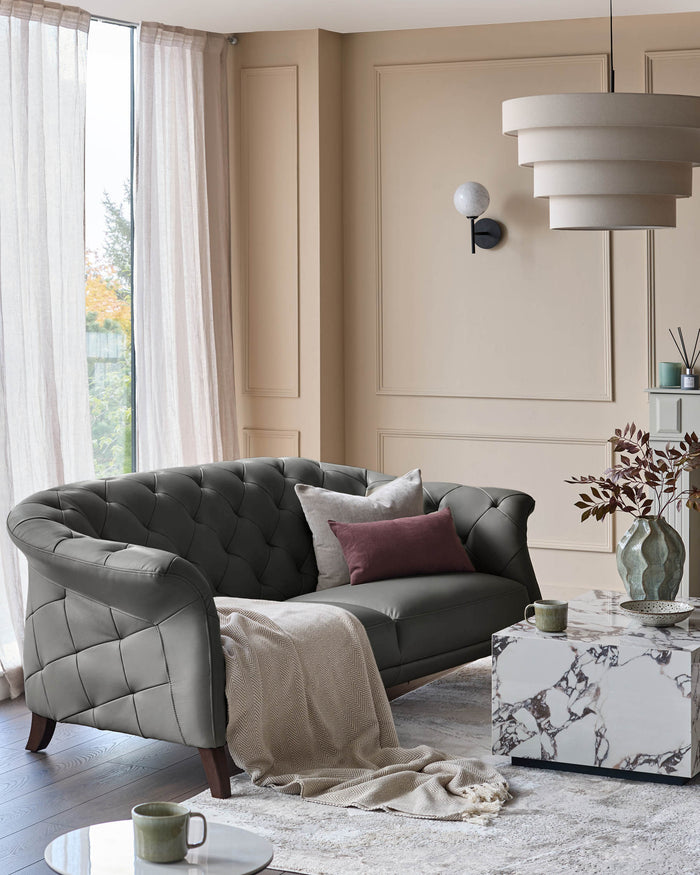 A stylish living room featuring a grey leather sofa, marble-topped tables and a tiered pendant light.