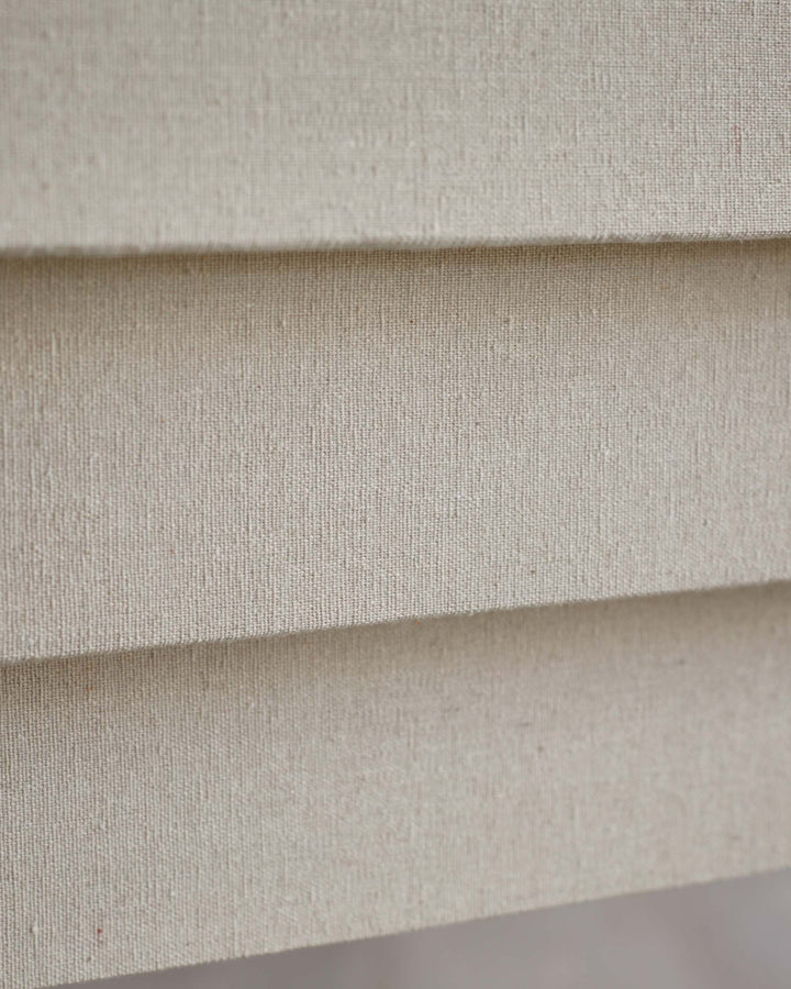 Close-up of layered, textured, beige fabric, potentially part of furniture such as blinds or upholstery.