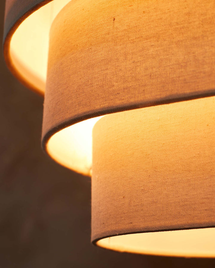 A tiered lampshade emits a warm glow, showcasing its textured fabric and inviting light in a cosy ambiance.