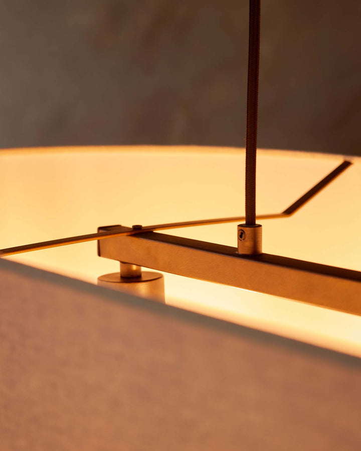 Close up on a modern light fitting with a brown cord and metal frame, emitting a warm light.