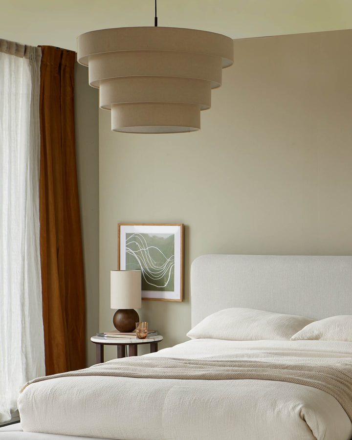 Bedroom featuring a bed with neutral bedding, side table with lamp, framed art and a layered lampshade.