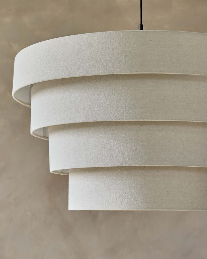 Close-up of a four-tiered, beige fabric lampshade hanging from the ceiling, showcasing a minimalist design and neutral colour palette.