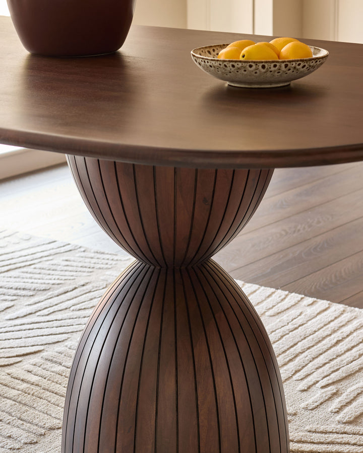 Dark mango wood round dining table with ribbed pedestal base and natural wood finish, styled with decorative bowl and lemons.