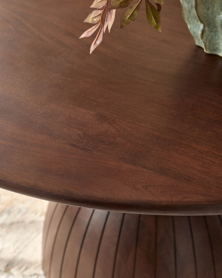 Dark mango wood dining table with ribbed pedestal base and decorative foliage detail on top surface.