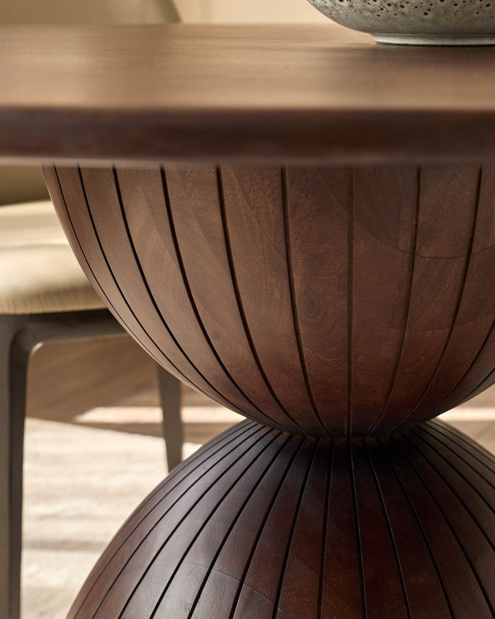 Dark mango wood dining table with vertical ribbed detailing on curved pedestal base, close-up side view.