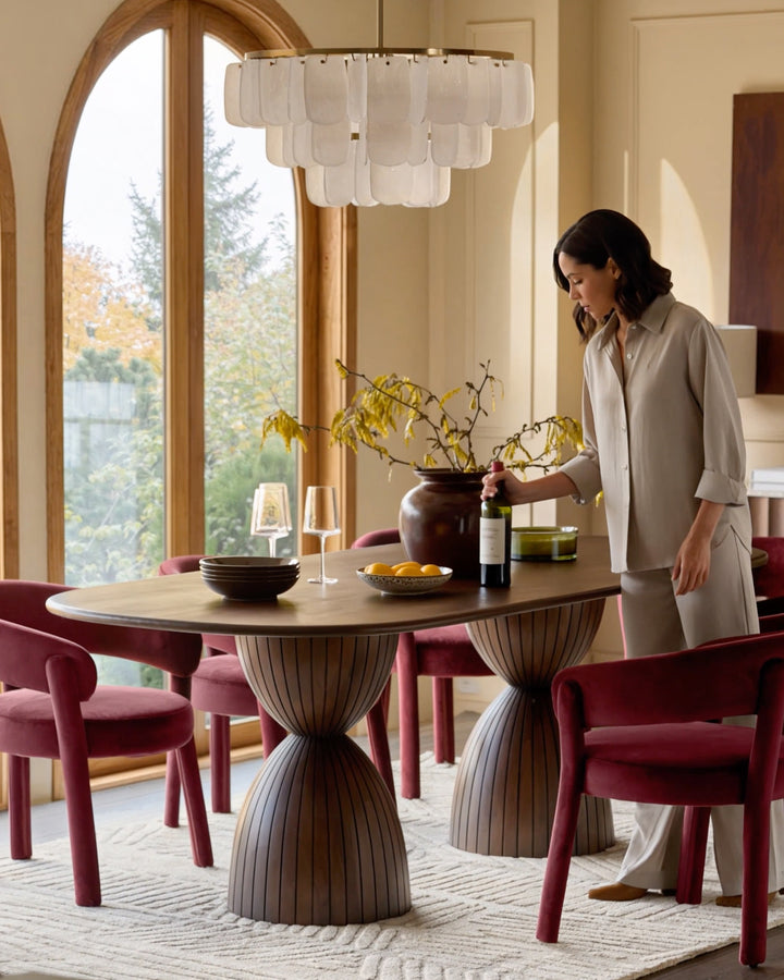 Dark mango wood round dining table with pleated pedestal base, styled with burgundy chairs in a bright dining room.