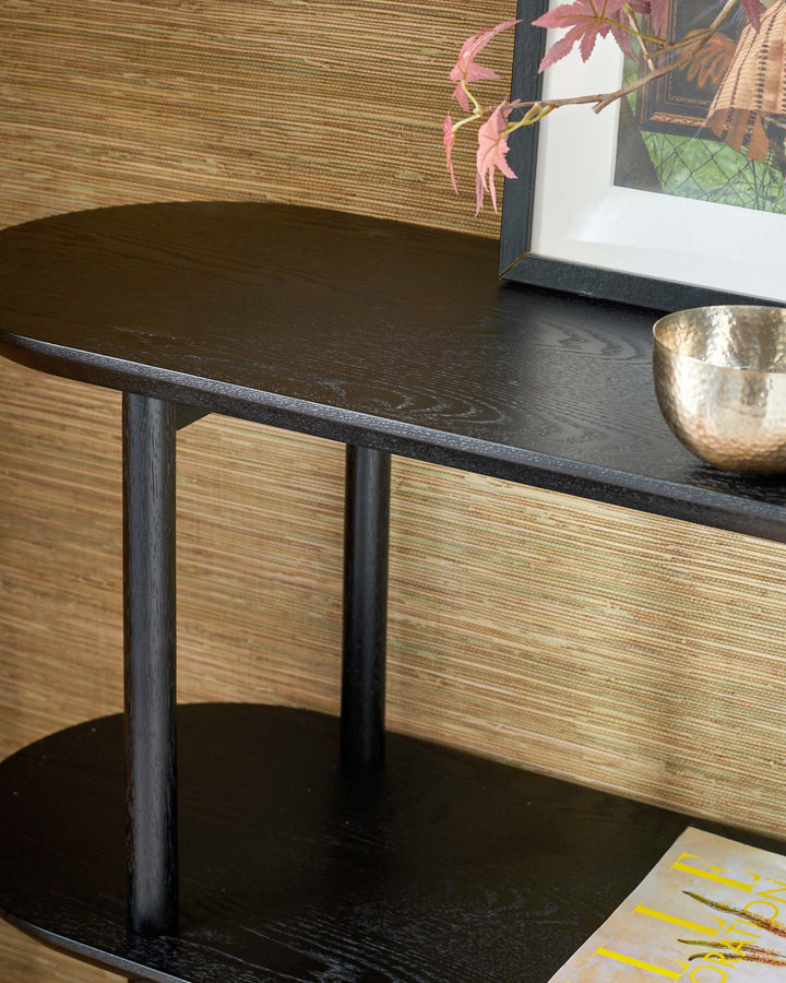 A dark, two-tiered side table with rounded shelves, displaying decorative items and a magazine.