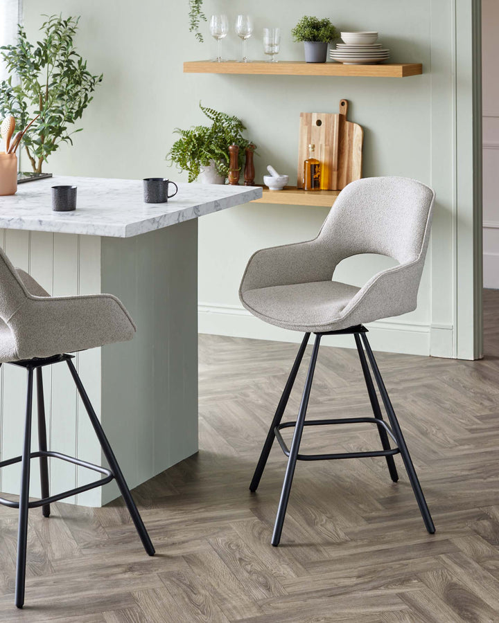 Modern upholstered bar stools with curved backrests and black, slender metal legs, positioned at a kitchen island with a marble countertop.