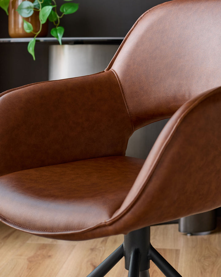 Tan leather swivel dining armchair with curved backrest and armrests, featuring a black metal base on wooden flooring.