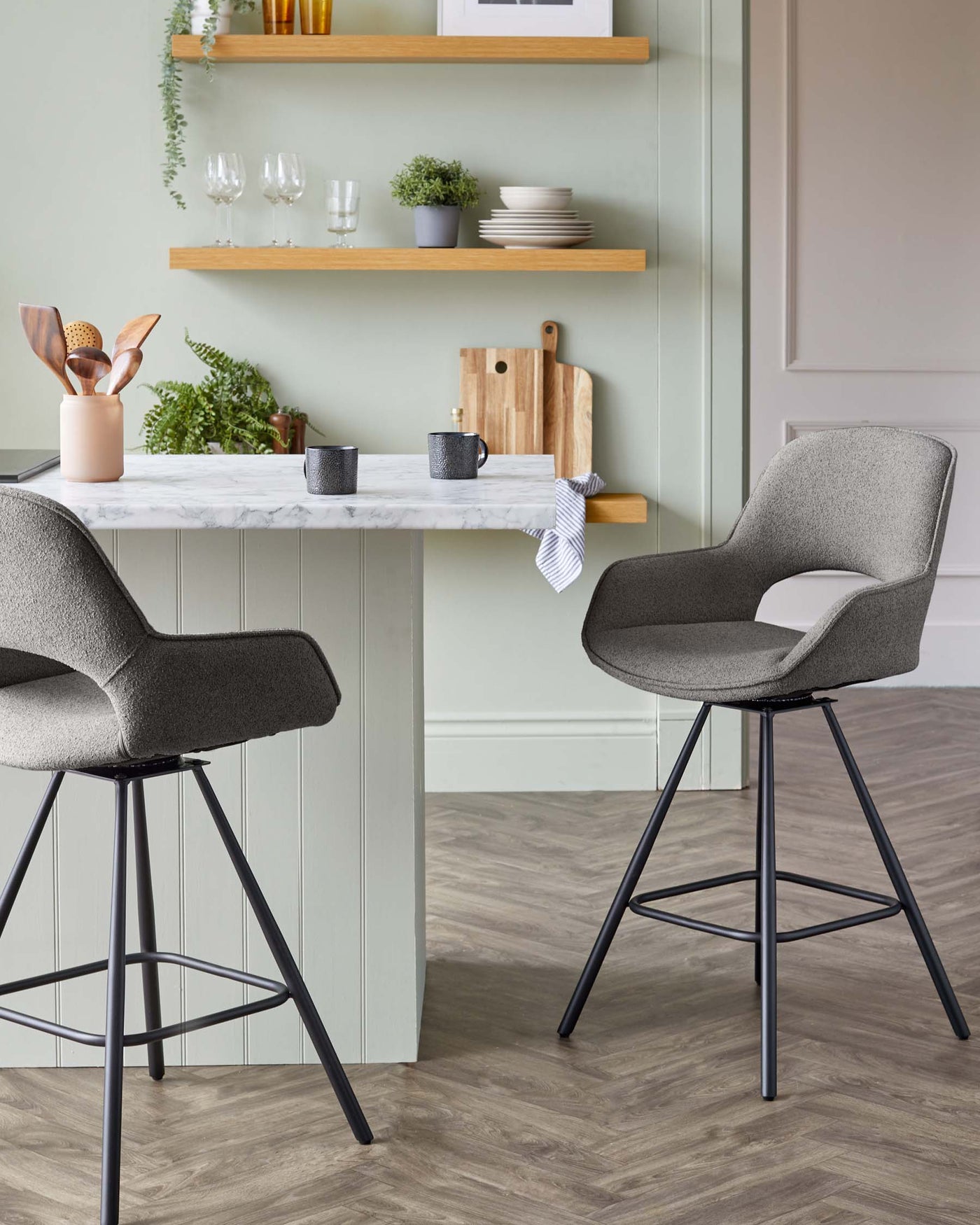 Two contemporary grey upholstered bar stools with black metal legs and a breakfast bar with a marble countertop and white panelled base.