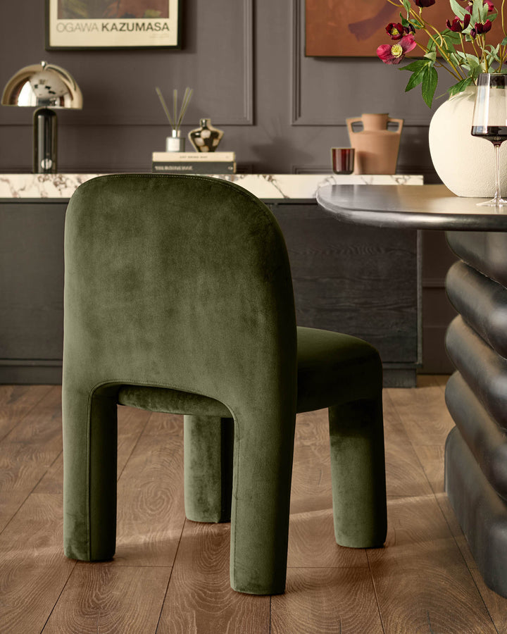 Mason dining chair in olive green velvet with curved cylindrical legs, shown in a styled dining room setting.