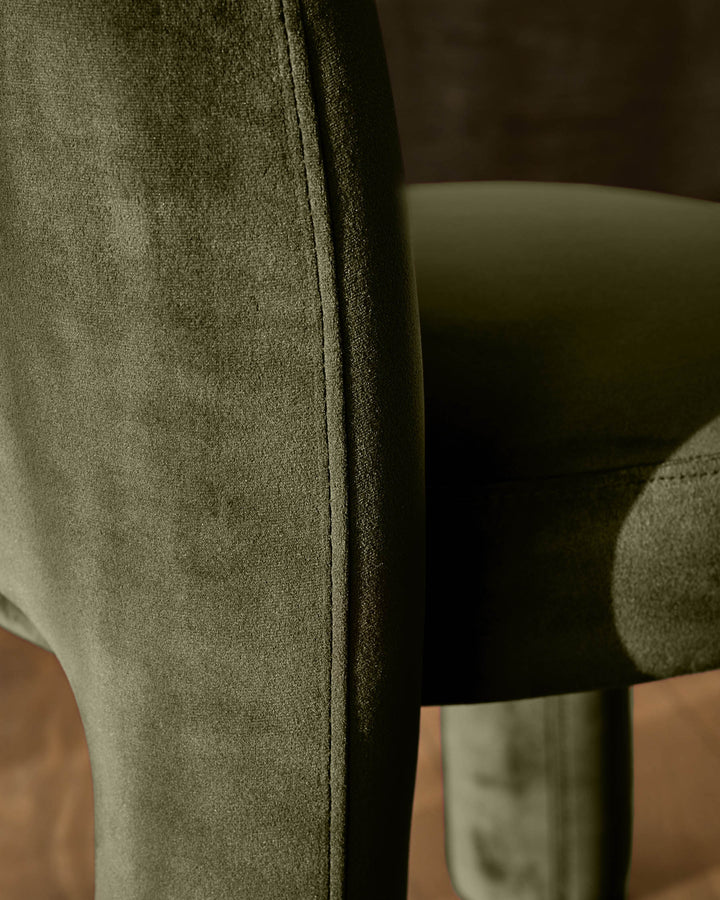 Mason dining chair in olive green velvet, close-up of backrest seam and curved armrest detail.