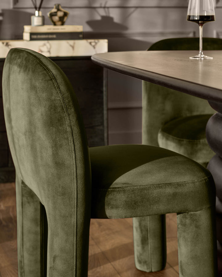 Mason dining chair in olive green velvet, shown from a side angle at a table setting with wine glass.