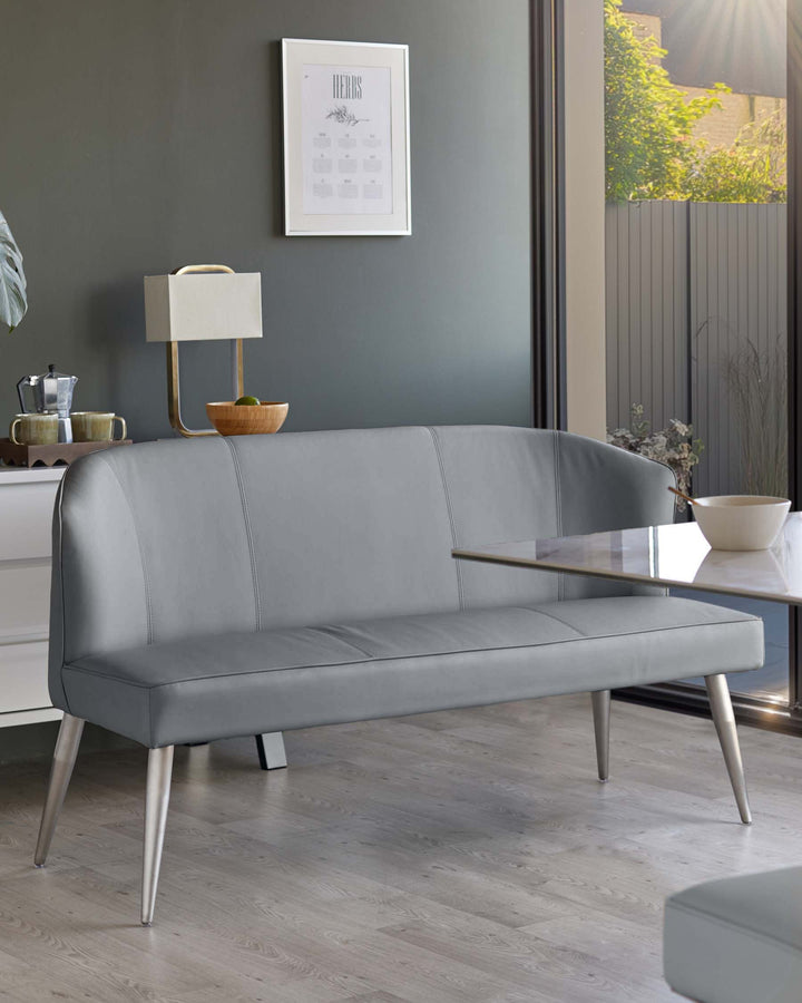 A modern grey faux leather dining bench with silver legs, positioned next to a marble-topped dining table.