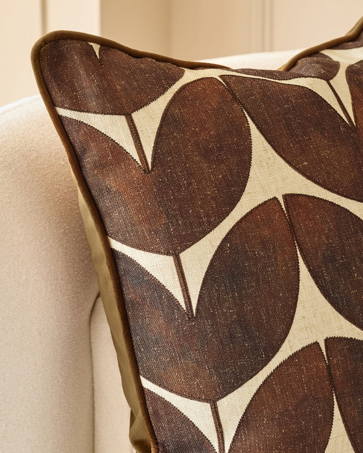 Micah Cushion in chocolate brown with cream geometric leaf pattern, piped edge detail, displayed on neutral sofa.