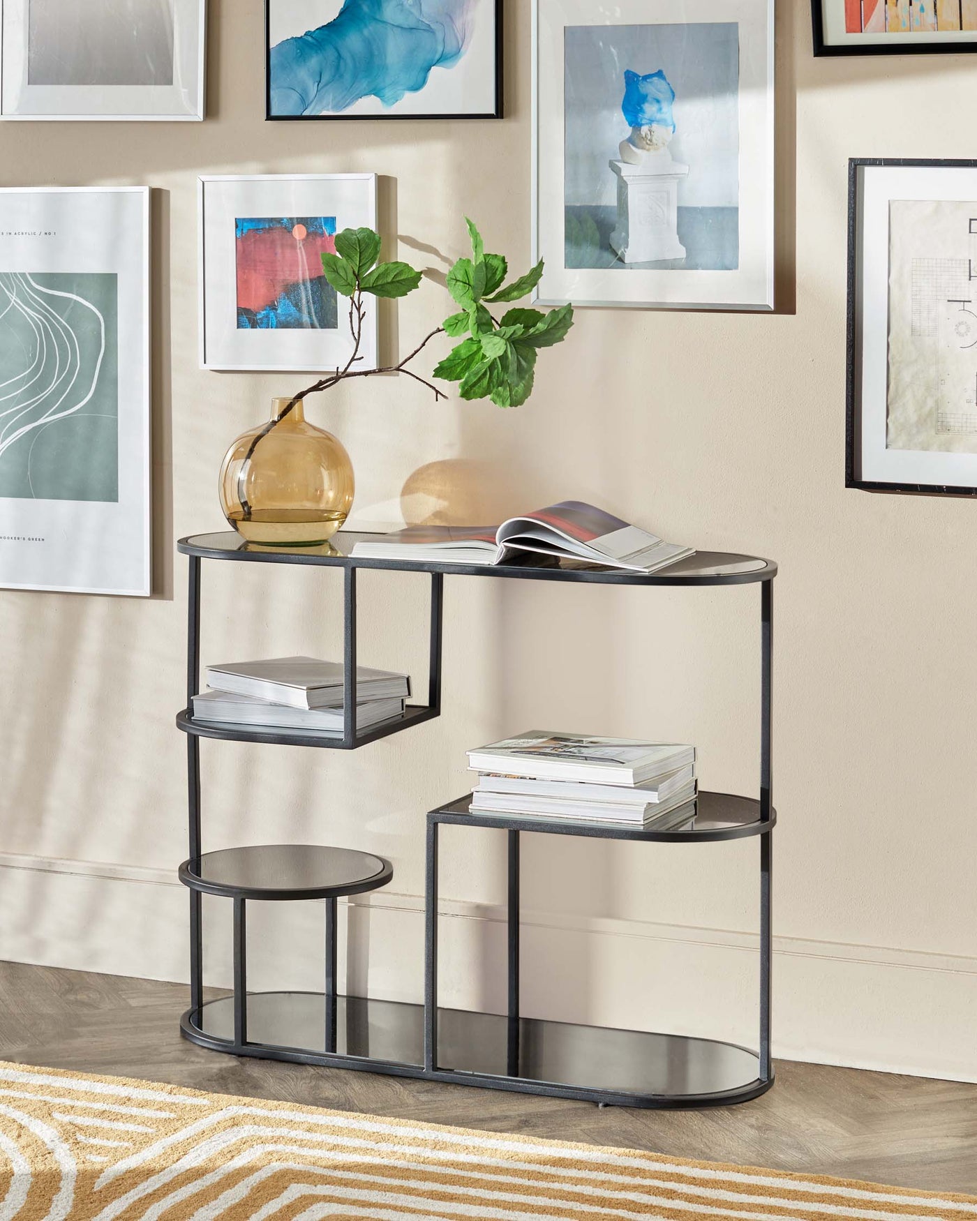 A modern asymmetrical metal and glass tiered console table with a semi-circular top, two rectangular shelves, and a smaller round side table attached at the bottom.