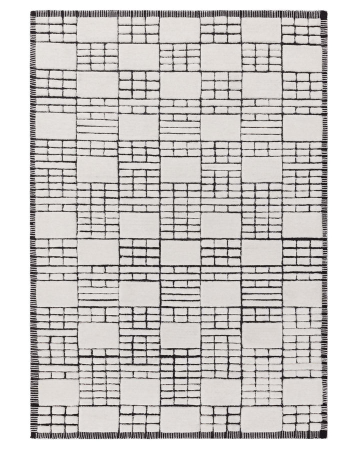Modern area rug with geometric block pattern in black and white, featuring a fringe detail at the edges.