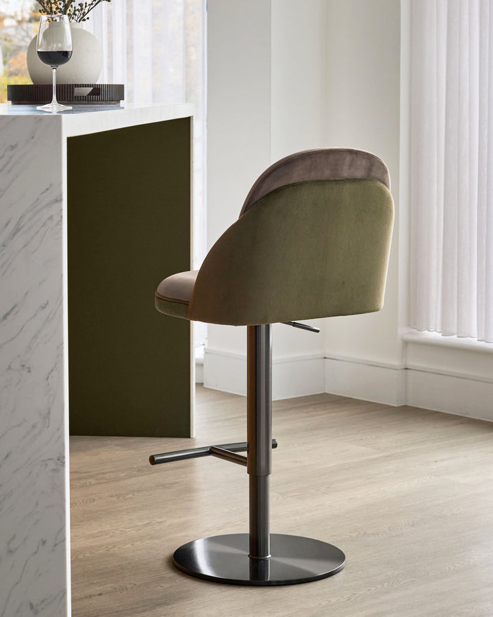 Myra gas lift bar stool in mocha and olive green velvet, shown from side angle with black metal base in modern room setting.