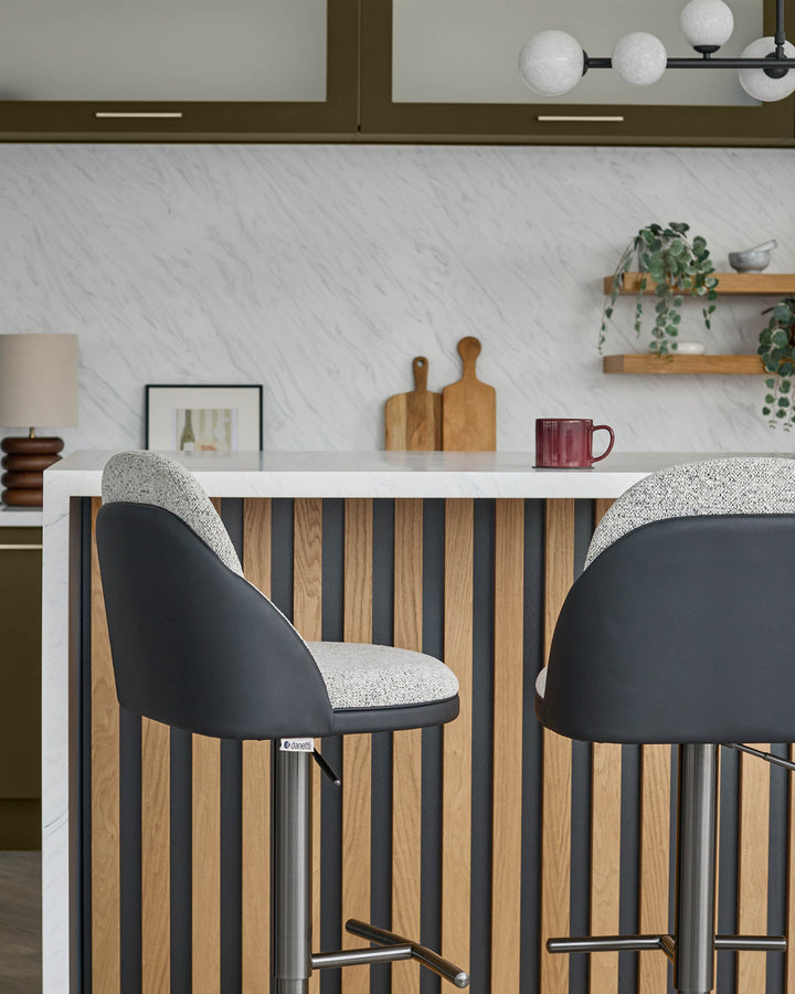Myra gas lift bar stools in grey fabric and black faux leather, shown at kitchen island with striped wood panel front.