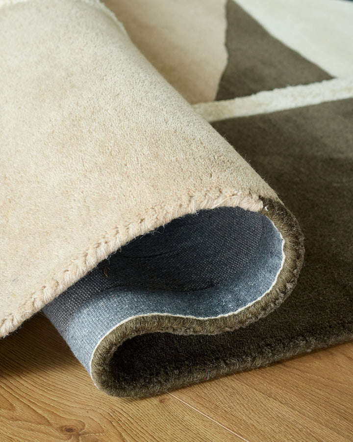 A modern rug is partly rolled to display its texture and backing on a wooden floor, showcasing its quality and design.