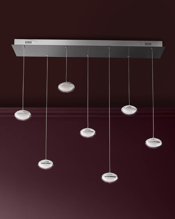 Nina 7-pendant light with round glass shades and chrome finish, suspended from rectangular canopy against burgundy wall.