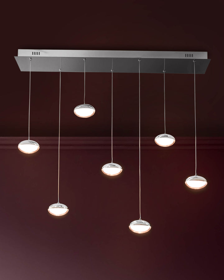 Nina 7-pendant light with silver chrome finish and glass shades, hanging from rectangular canopy against burgundy wall.