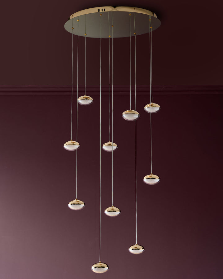 Nina 10-pendant light with soft gold finish and frosted glass shades suspended from ceiling canopy against burgundy wall.