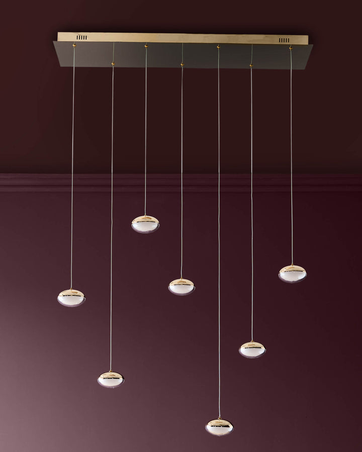 Nina 7-pendant light with soft gold finish and frosted glass shades, suspended from a rectangular canopy against a burgundy wall.