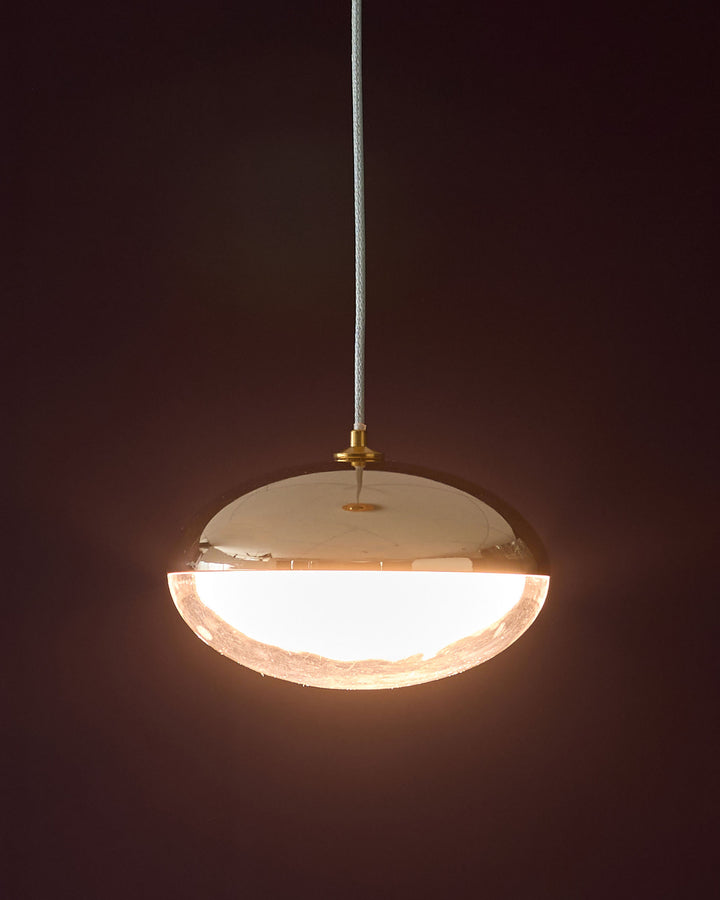 Nina single pendant light in soft gold with frosted glass bowl, suspended by white cord against dark background.