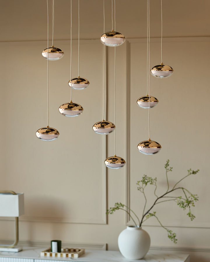 Nina 10-pendant light in soft gold finish with clear glass bowls, hanging at varying heights in a modern interior setting.