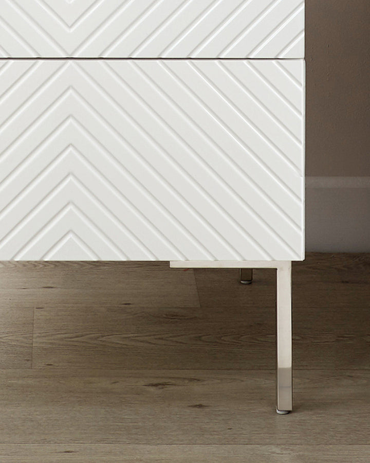 Noah white bedside table with chevron drawer fronts, metal legs, side view on wood flooring.