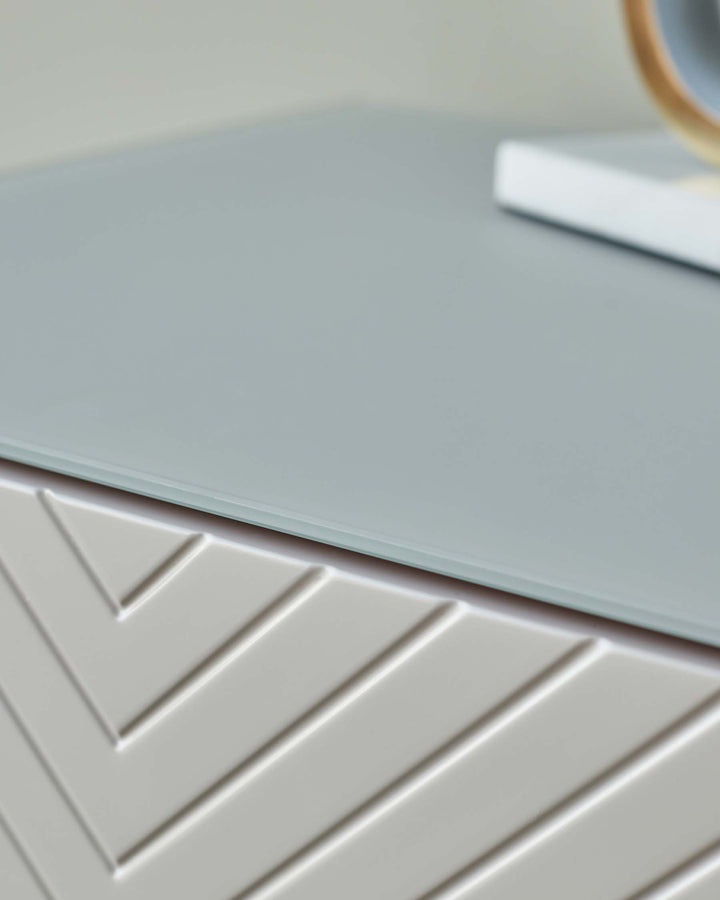 A stylish grey bedside table with chevron pattern and glass top.