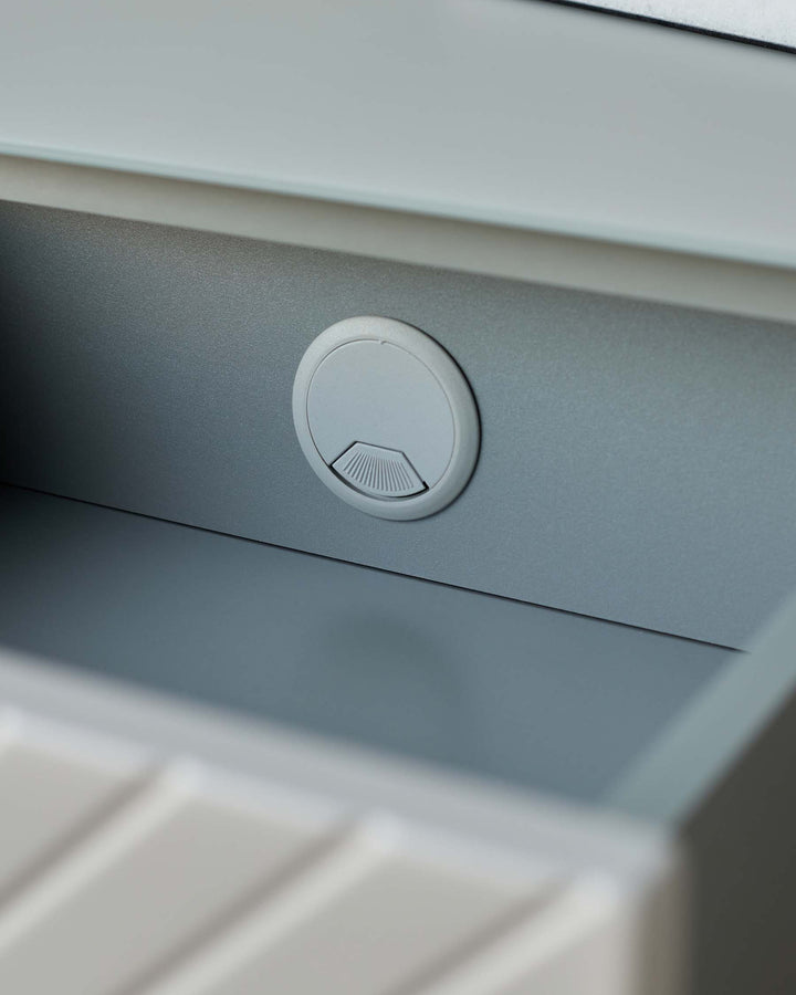 Close up of a grey desk featuring a circular cable tidy with a fan detail. Office or home working furniture.