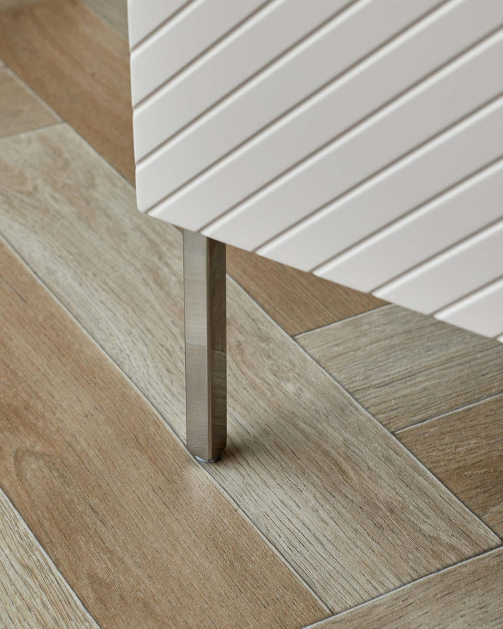 Contemporary furniture with a slatted design, standing on sleek, metal legs atop a light wood-effect herringbone floor.
