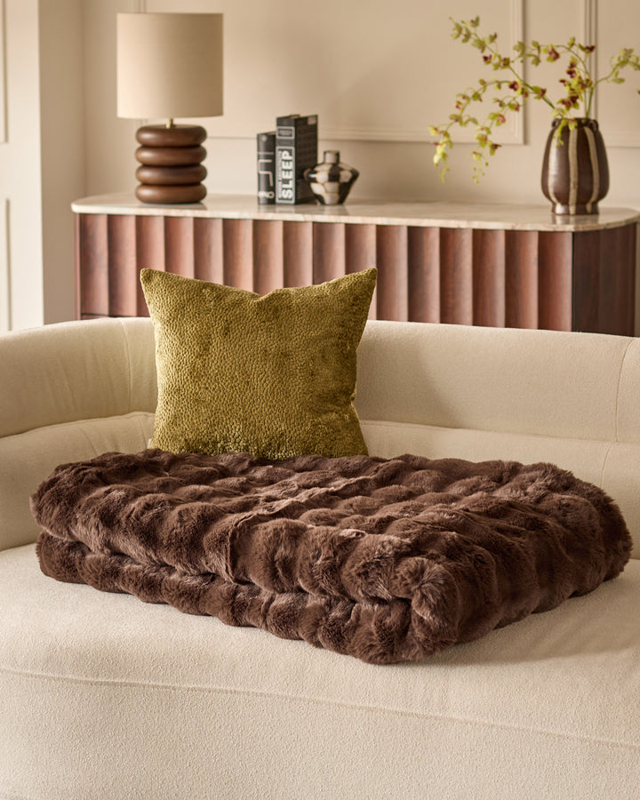 Harlene cushion in olive green displayed on a cream sofa with brown faux fur throw blanket, styled in modern living room setting.